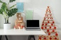 Christmas online shopping. Laptop and gifts on a white desk, original Christmas tree from branches in a home office.