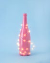 Christmas pastel pink bottle with shining neon, new year lights. Winter party concept on pastel blue background