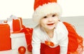 Christmas and people concept - cute smiling child in santa red hat with boxes gifts