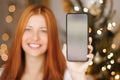 Christmas phone call and holiday greeting concept. Happy smiling woman showing screen of mobile smartphone, xmas