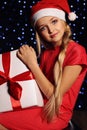 Christmas photo of cute little blond girl in santa hat and red dress holding a gift - box Royalty Free Stock Photo