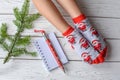 A Christmas photo with feminine feet in bright red socks, a fir twig, a note book and a pencil on a white wooden floor