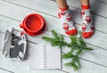 A Christmas photo with a girl`s feet in bright red socks, a fir twig, a note book and a pencil on a white wooden floor Royalty Free Stock Photo