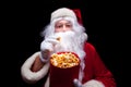 Christmas. Photo of Santa Claus gloved hand With a red bucket with popcorn, on a black background Royalty Free Stock Photo