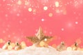 Christmas pink background with golden star. New Year`s decor. Christmas balls in smowdrifts and golden bokeh lights