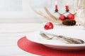 Christmas place setting with white dishware, cutlery, silverware and red decorations on wooden board. Christmas Royalty Free Stock Photo