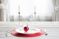 Christmas place setting with white dishware, cutlery, silverware and red decorations on white. Royalty Free Stock Photo