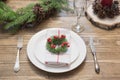 Christmas place setting with white dishware, silverware and decorations on wooden board. Christmas wreath as decor. Royalty Free Stock Photo