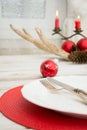 Christmas place setting with white dishware, silverware and red decorations on white board in interior near the window. Royalty Free Stock Photo