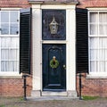 Christmas porch with christmas wreath and street light. House facade with vintage front door, antique shuttered windows. Black Royalty Free Stock Photo