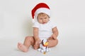 Christmas portrait of charming little baby boy, wearing santa hat, playing with little cute plastic dog toy, infant studying new