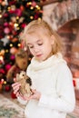 Christmas portrait of happy blonde child girl in white sweater holding toy owl near the Christmas tree and wooden toy horse. New Y Royalty Free Stock Photo