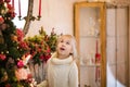 Christmas portrait of happy blonde child girl in white sweater siting on the floor near the Christmas tree and wooden toy horse. N Royalty Free Stock Photo