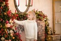 Christmas portrait of happy blonde child girl in white sweater siting on the floor near the Christmas tree and wooden toy horse. N Royalty Free Stock Photo