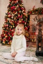 Christmas portrait of happy blonde child girl in white sweater siting on the floor near the Christmas tree and wooden toy horse. N Royalty Free Stock Photo