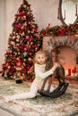 Christmas portrait of happy blonde child girl in white sweater siting on the floor near the Christmas tree and wooden toy horse. N Royalty Free Stock Photo