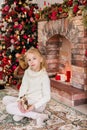 Christmas portrait of happy blonde child girl in white sweater siting on the floor near the Christmas tree and wooden toy horse. N Royalty Free Stock Photo