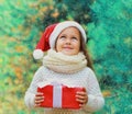 Christmas portrait happy smiling little girl child in santa red hat with gift box near a green branch tree Royalty Free Stock Photo