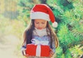 Christmas portrait happy smiling little girl child in santa red hat with gift box near a green branch tree Royalty Free Stock Photo