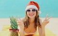 Christmas portrait of happy young smiling woman in red santa hat with funny pineapple lying on a beach together over sea Royalty Free Stock Photo
