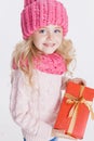 Christmas. Portrait of little curly girl in knitted pink winter hat and scarf on white. Red Present in her Royalty Free Stock Photo