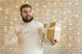 Christmas portrait of middle adult bearded man with gift box in studio room with garland lamps on white brick wall background