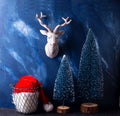 Christmas  postcard - Santa Claus hat in wire basket, two decorative blue trees  and deer Royalty Free Stock Photo