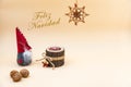 Christmas postcard with text Feliz Navidad and a beige background, nuts, wooden candle and a funny gnome