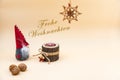 Christmas postcard with text Frohe Weihnachten and a beige background, nuts, wooden candle and a funny gnome