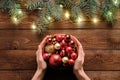 Christmas preparation concept. Female hands holding bowl with red baubles decoration over rustic wooden background with fir tree Royalty Free Stock Photo