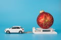 Christmas preparations concept. Close up photo of toy mini car carrying white wooden sledge with red golden ornament bauble on top Royalty Free Stock Photo