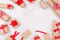 Christmas preparations - packaging gifts boxes in kraft paper with red bows and ribbons, twine on white wood table, frame.