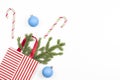 Christmas present gift bag with fir tree branch, candy canes and blue Xmas decoaration baubles balls on white background