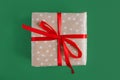 Christmas present wrapped in craft polka dot paper with red ribbon on green background Royalty Free Stock Photo