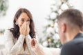 Christmas proposal by a man holding a ring in front of his surprised girlfriend