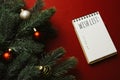 Christmas red background with blank notebook with wish list, pen, fir branches and red decorations. Christmas, New Year