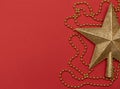 Christmas red background with golden star - the top of Christmas tree and golden beads. Flat lay style. Royalty Free Stock Photo