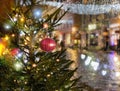 Christmas red ball  festive holiday street decoration green tree branch people walk with umbrella evening blurred light medieval Royalty Free Stock Photo