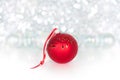 Christmas red ball on red ribbon on background of shiny tinsel, white bolls, lights and sparkles bokeh close up Royalty Free Stock Photo