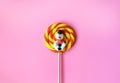 Christmas round spiral orange, yellow lollipop candy on a stick on pink background. Sugar snowman. Royalty Free Stock Photo