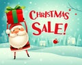 Christmas Sale! Santa Claus holds up gift present in Christmas snow scene winter landscape. Royalty Free Stock Photo