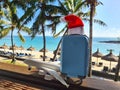 Christmas Santa Claus red hat on handle travel luggage with tropical beach and turquoise sea background Royalty Free Stock Photo