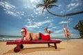 Christmas Santa Claus resting on sunlounger at ocean sandy tropical beach and two Beautiful women swinging Royalty Free Stock Photo