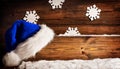 Christmas Santa Hat hanging on Wooden Board Sign. Blue Claus Cap over brown Grunge Wood Background with Snow and Snowflakes. Xmas Royalty Free Stock Photo