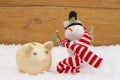 Christmas Savings, Piggy Bank and Snowman with scarf on snow wi Royalty Free Stock Photo