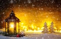 Christmas scene with a lantern, trees, fir branch, snow flakes and blurred lights in front of an illuminated dark wooden board as Royalty Free Stock Photo