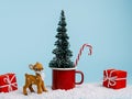 Christmas scene with red cup, pine tree, snow and small deer on pastel blue background. Creative Xmas or New Year festive concept. Royalty Free Stock Photo