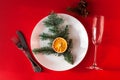 Christmas served dinner, meal table design on red background. White plate, champagne glass, fir, dried orange and decorations. New Royalty Free Stock Photo