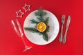 Christmas served dinner, table design on red background. White plate, champagne glass, fir, star, dried orange, fork, knife. New