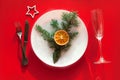 Christmas served dinner, table design on red background. White plate, champagne glass, fir, star, dried orange, fork, knife. New